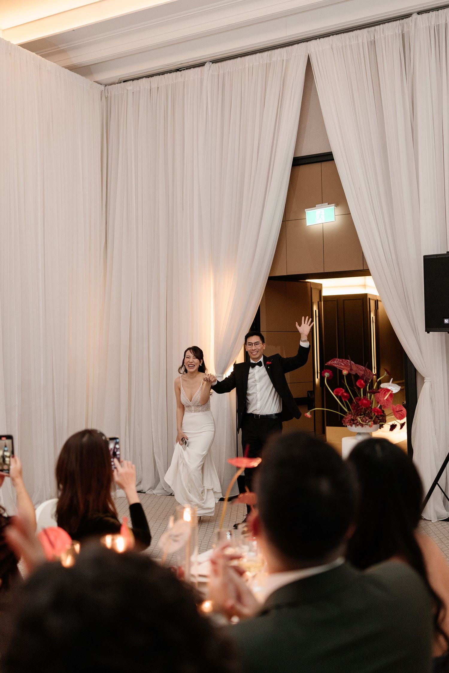 Bride and groom make a grand entrance through white draped curtains at their wedding reception.