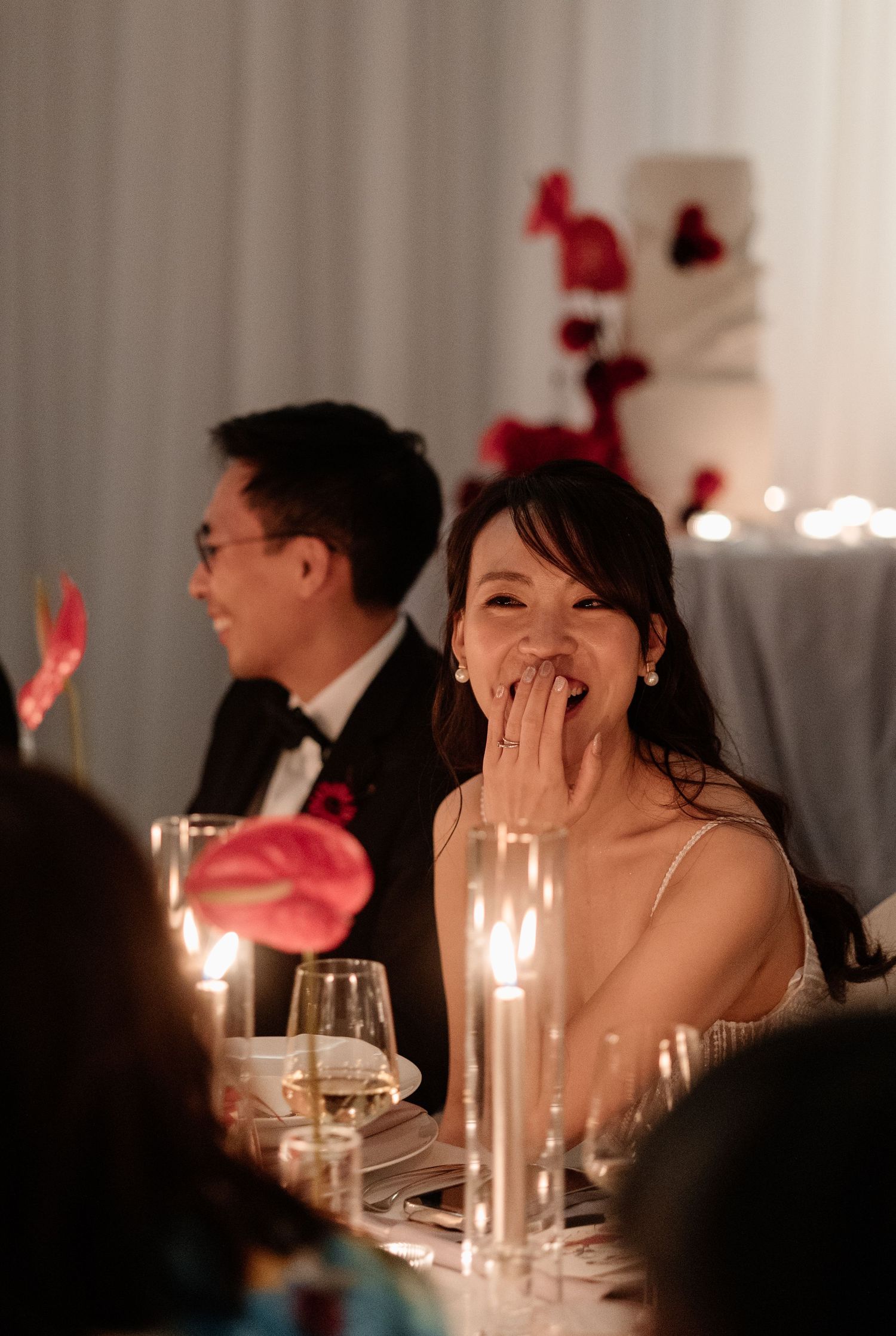 Radiant bride laughing joyfully at the sweetheart table during her candlelit wedding reception.