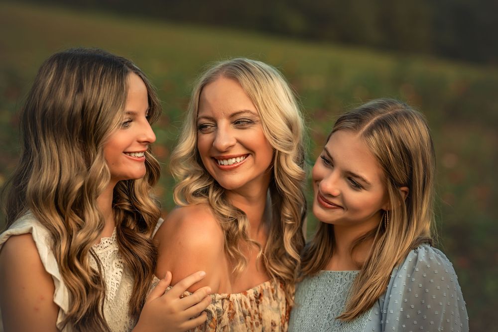 Mom and two daughters with long hair posing together outdoors in warm golden sunset light.