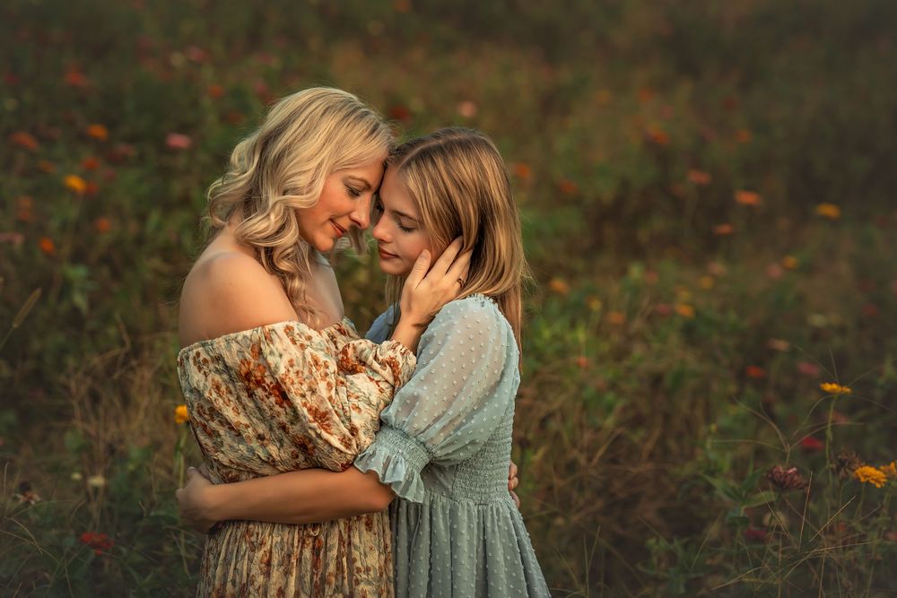Mother and daughter sharing a tender forehead-to-forehead moment in a blooming flower field at sunset.