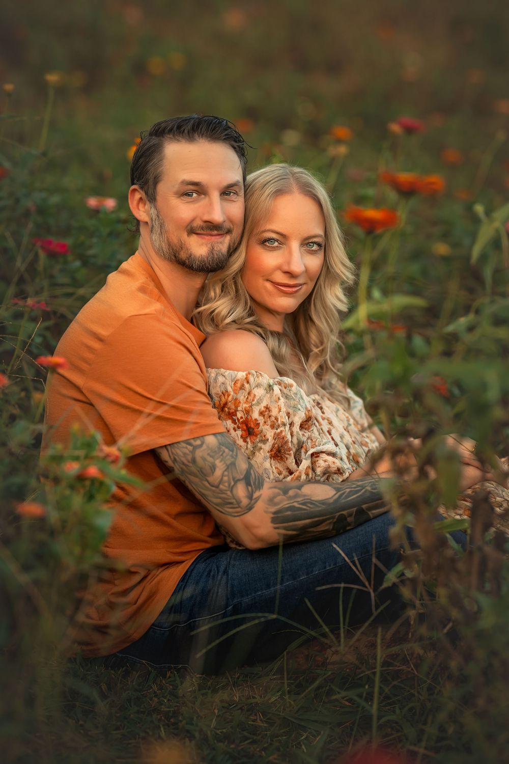 Couple embracing in a flower field at golden hour, man in orange shirt hugging woman in floral dress.