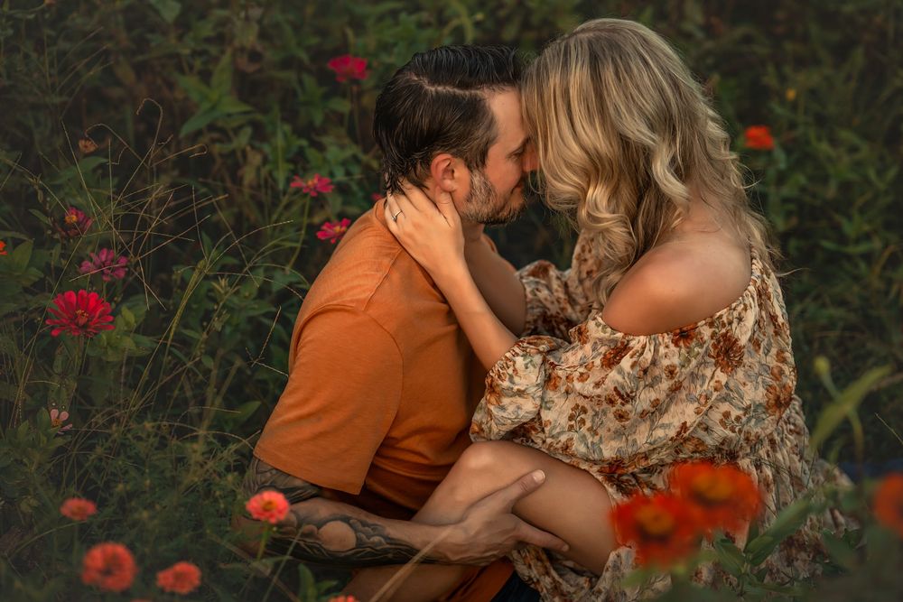 A couple shares a romantic moment surrounded by vibrant red flowers in a lush garden setting.