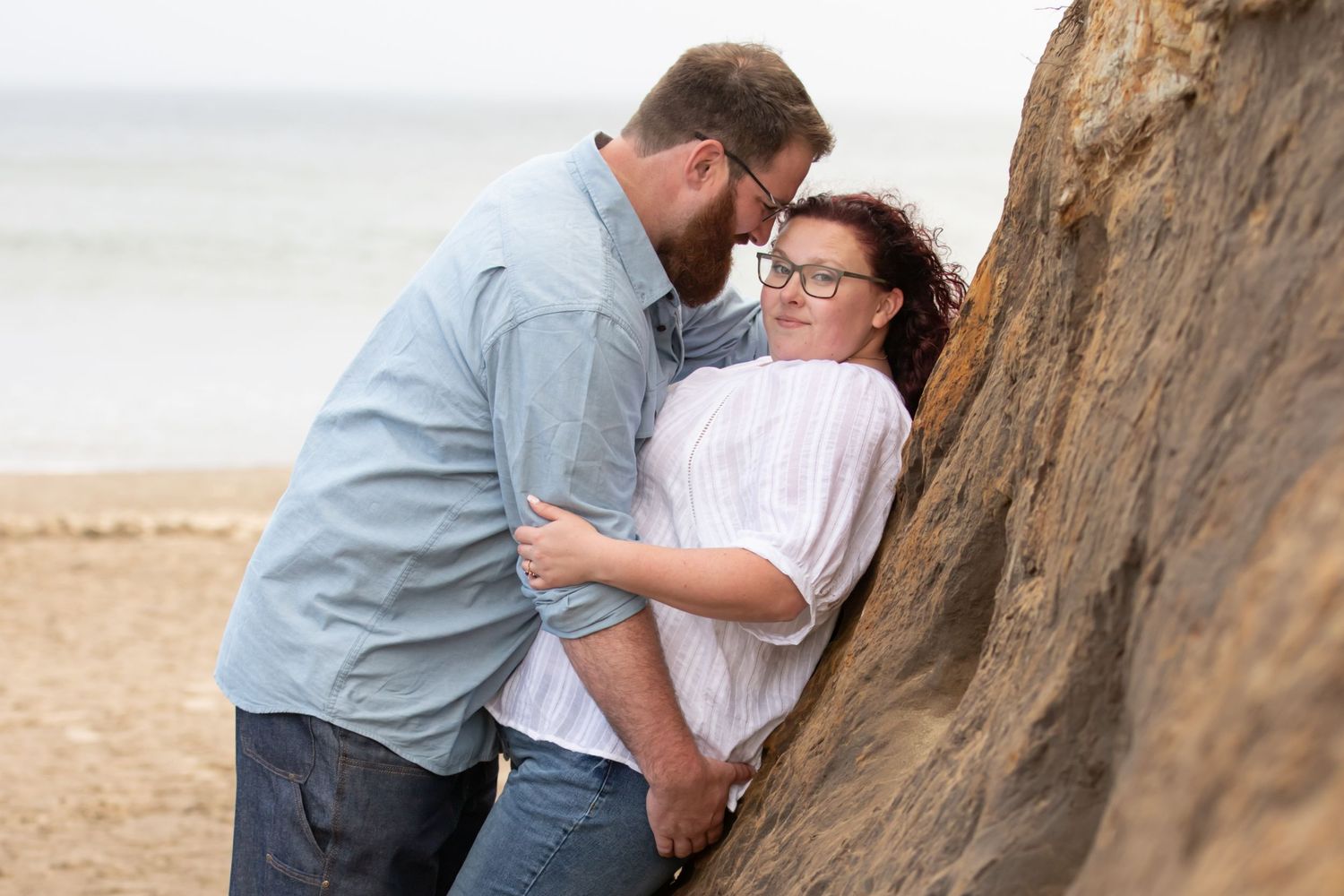 Intimate couple moment against rustic brick wall wearing matching white shirts and jeans.