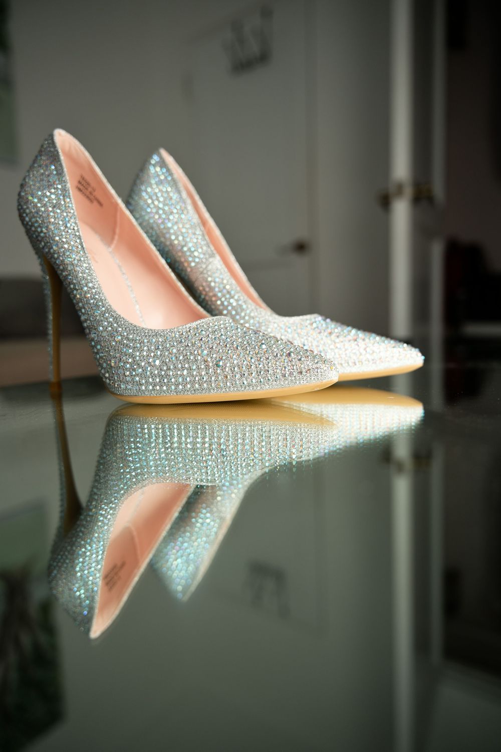 Crystal-encrusted silver stiletto heels reflected on a glass surface, perfect for a glamorous wedding or formal event.