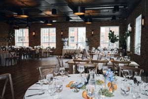 Elegant wedding reception venue with round tables, white linens, floral centerpieces, brick walls, and industrial pendant lights.