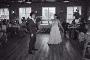 Black and white photo of a bride and groom sharing their first dance at a wedding reception in a rustic venue.