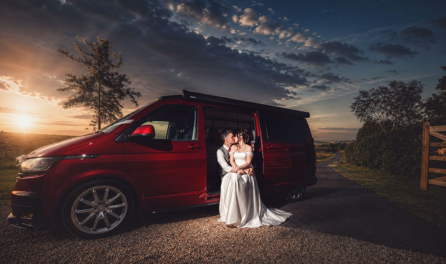 Bride and groom kissing beside a red VW van at sunset during their wedding day outdoor photo shoot.