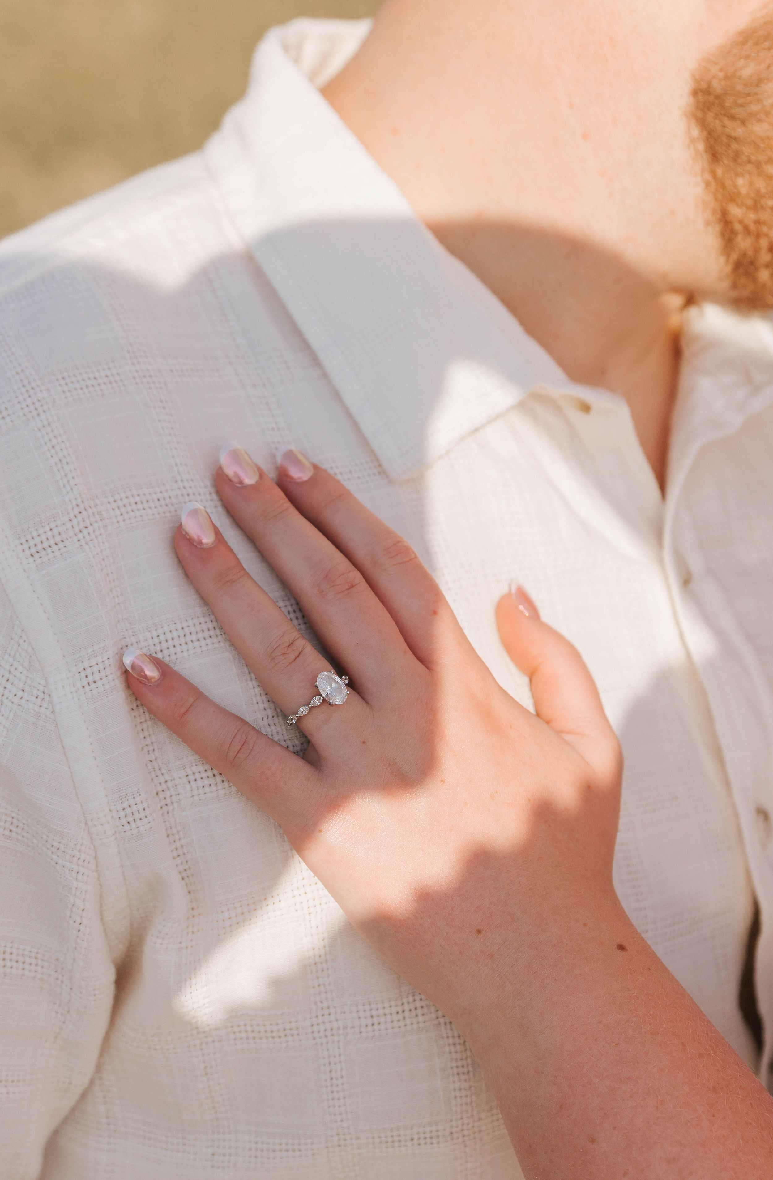 Close-up of a woman's hand with French manicure nails wearing a diamond engagement ring, resting on a man's white shirt.