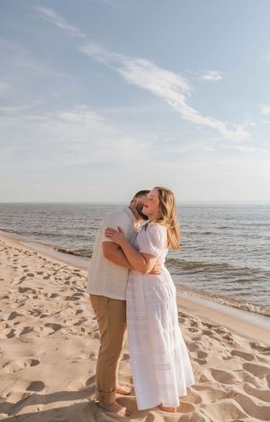 Couple sharing a romantic kiss on a sandy beach with calm ocean waves and blue sky in the background.