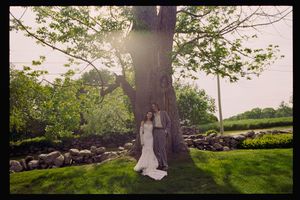 Bride and groom posing under a large tree in a lush green garden on their wedding day.