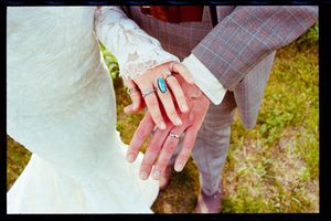 Bride and groom showing wedding rings, woman wearing turquoise ring, white lace dress and gray plaid suit.