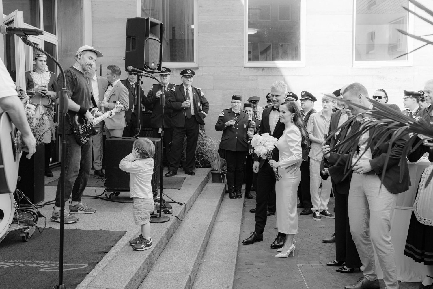 Black and white photo of a outdoor gathering with musicians performing on steps while a crowd watches nearby.