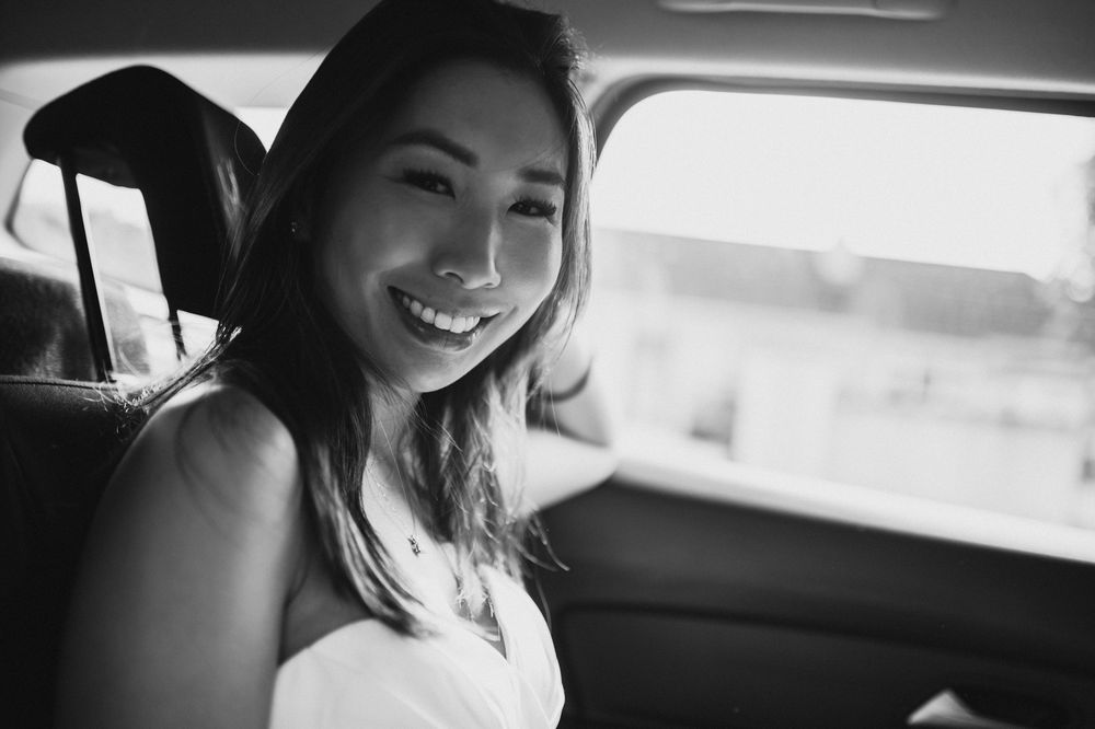 Smiling young woman sitting in backseat of car, black and white portrait photo.