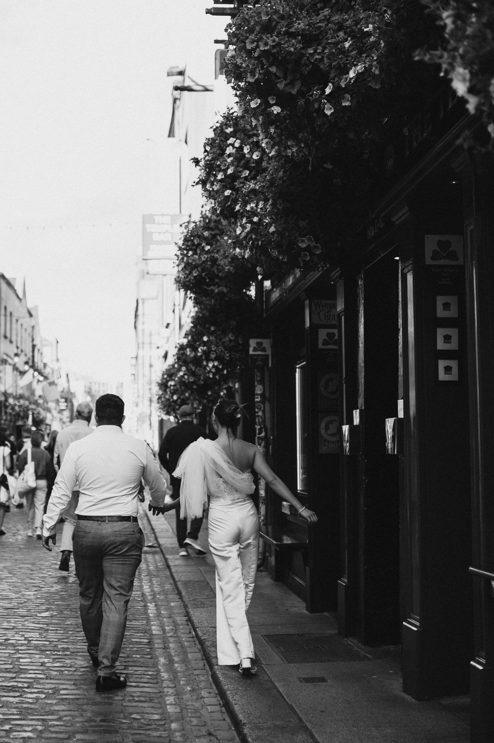 Couple walking hand in hand down a cobblestone street in black and white photography.