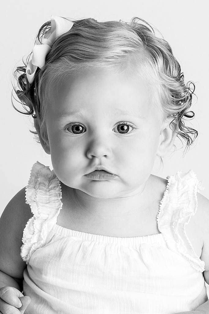Black and white portrait of a curly-haired baby girl with a bow in her hair.