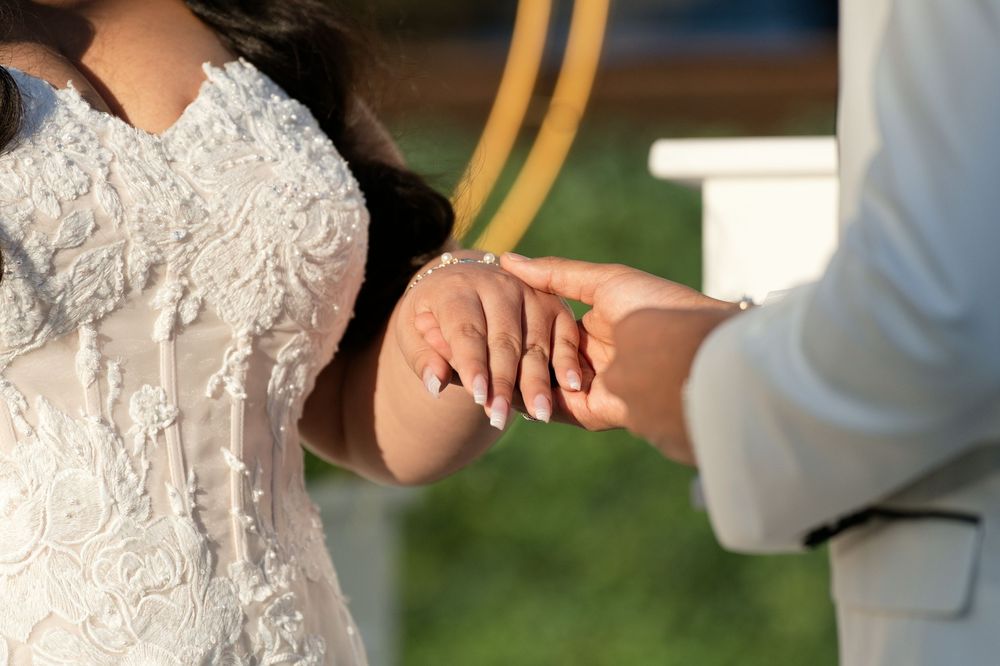 Bride and groom exchanging rings during wedding ceremony, close-up of hands in elegant white attire.
