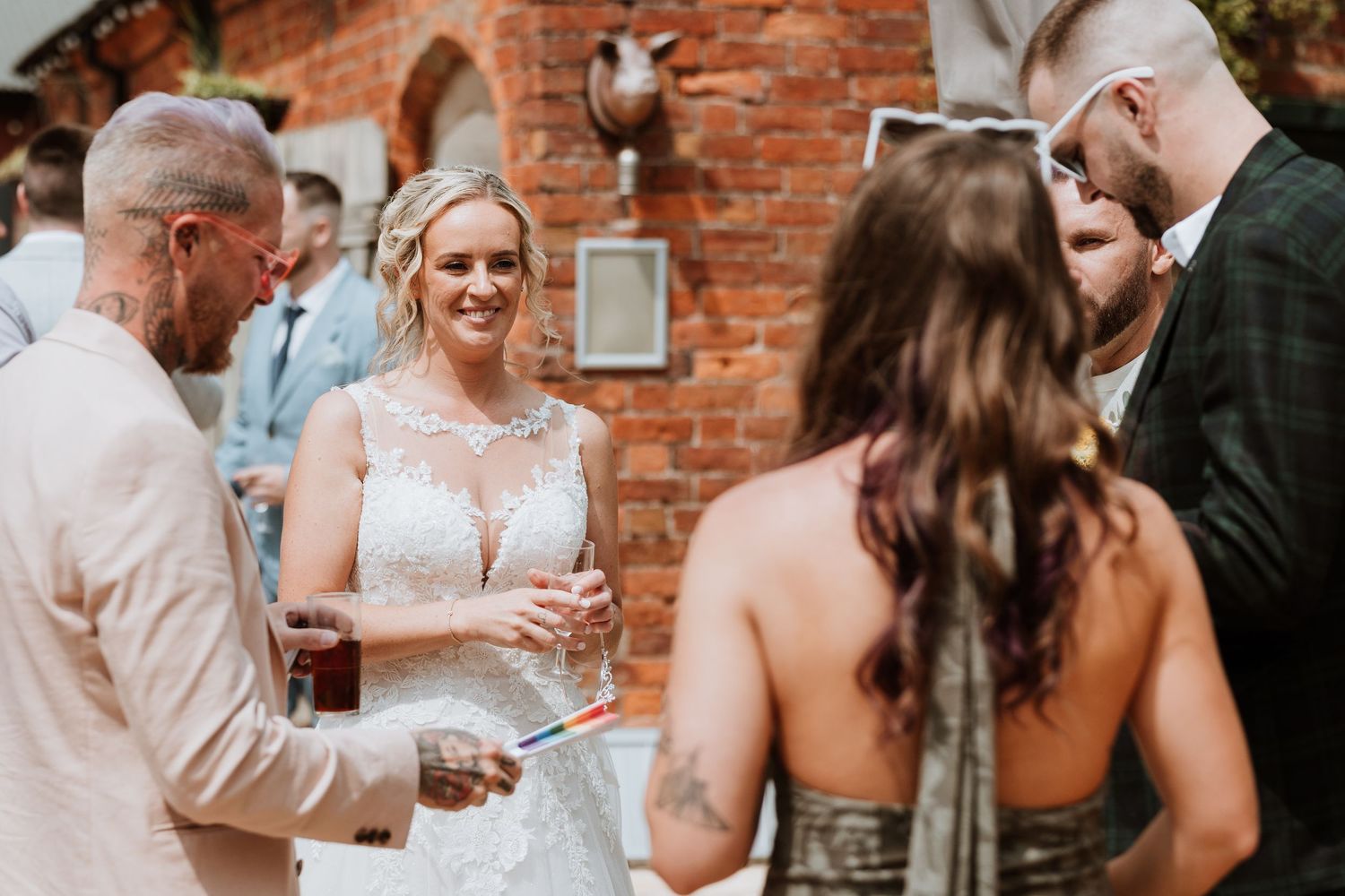 Bride in lace wedding dress smiling and socializing with guests outdoors at a brick venue wedding reception.