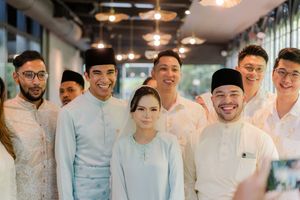Group of people in traditional Malay attire posing together at a formal indoor event.