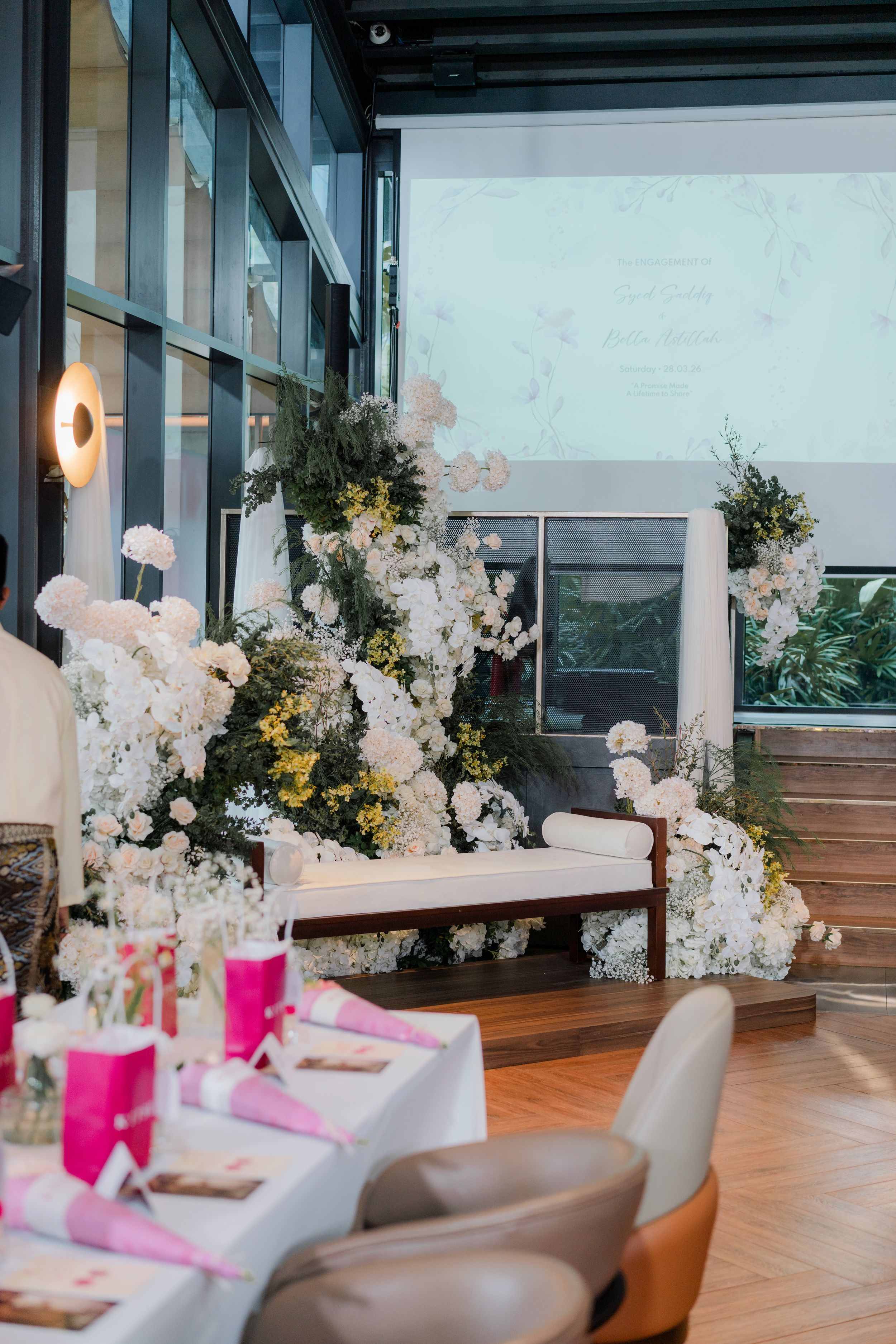 Elegant wedding reception venue with white floral arch, pink table settings, and projection screen backdrop.