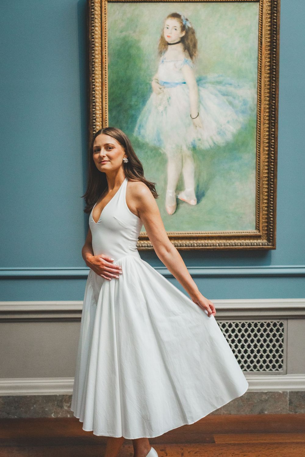 Woman in white dress posing in front of Renoir ballet dancer painting in art museum.