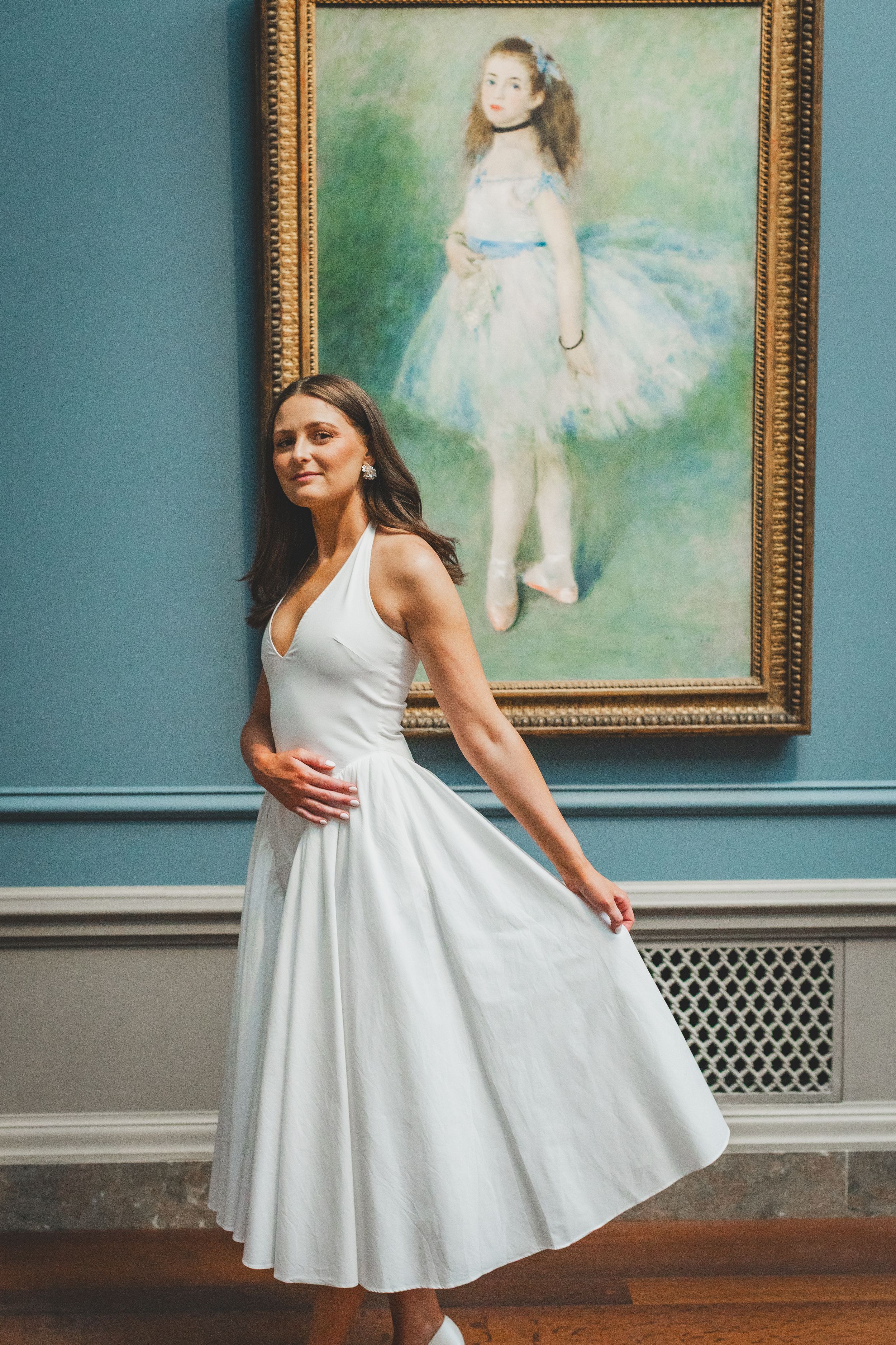 Woman in white dress posing in front of Renoir ballet dancer painting in art museum.