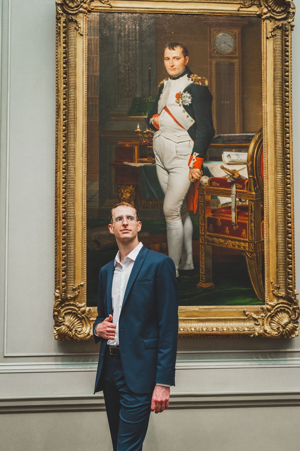 Man in blue suit standing before a framed Napoleon Bonaparte portrait painting in a museum gallery.