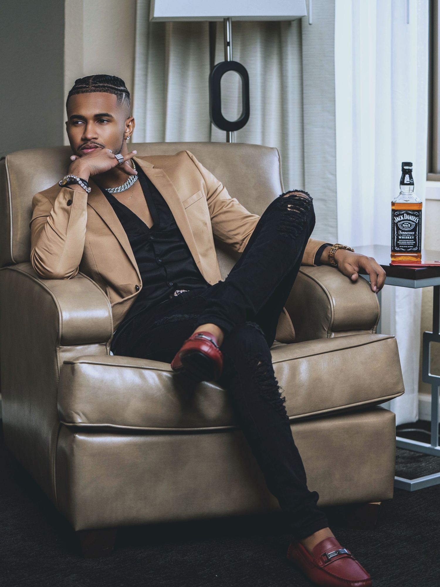 A stylish man in a black pinstripe suit holds a professional camera with a telephoto lens while seated on a sofa.