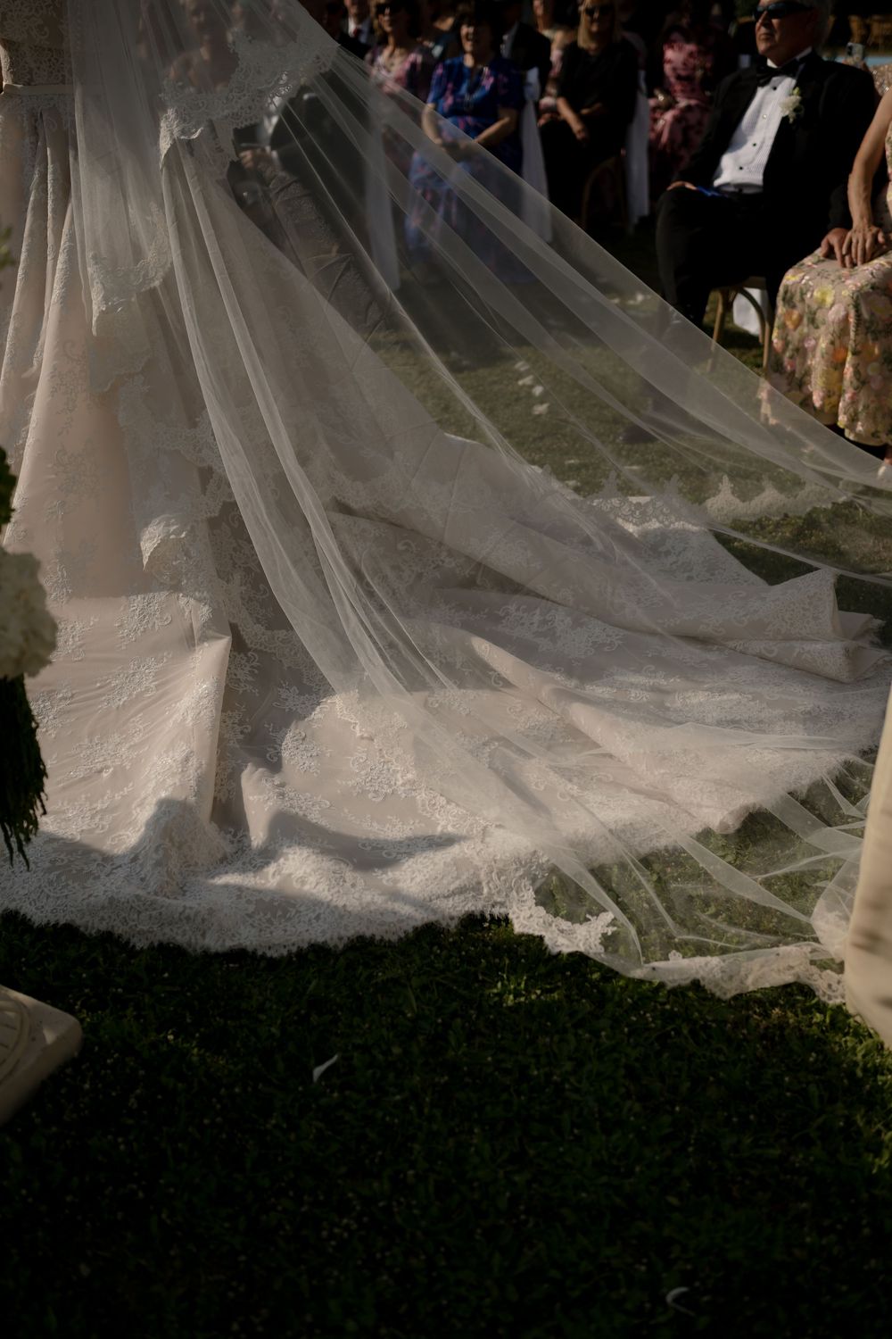 Elegant lace wedding dress train and veil spread across grass during outdoor ceremony.