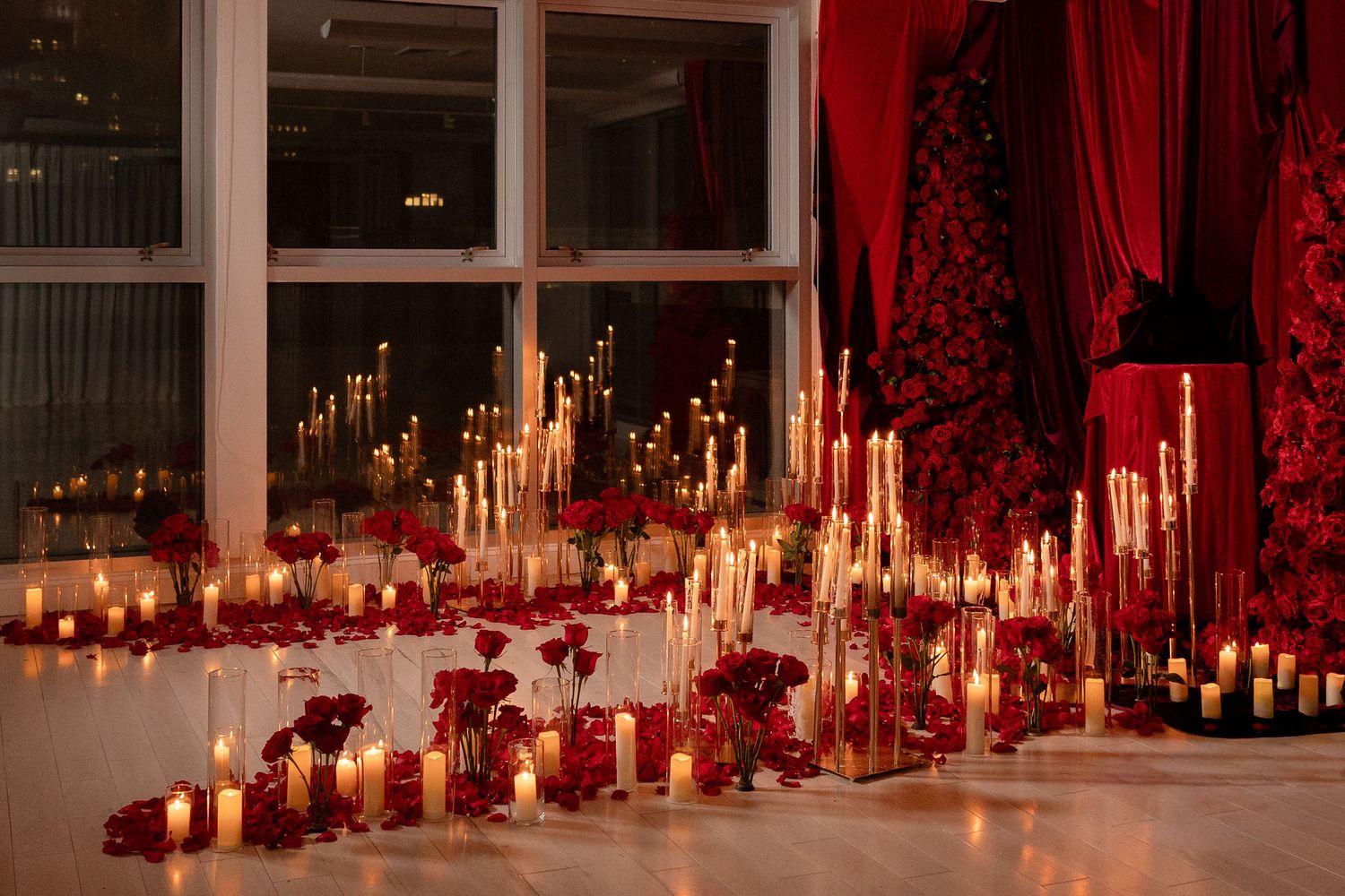 Romantic red and white candlelit wedding reception with roses, tall tapers, and lush floral arrangements on a reflective floor.