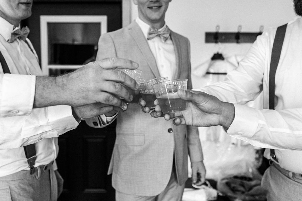 Groomsmen in bow ties clinking glasses in a celebratory toast during wedding preparations.