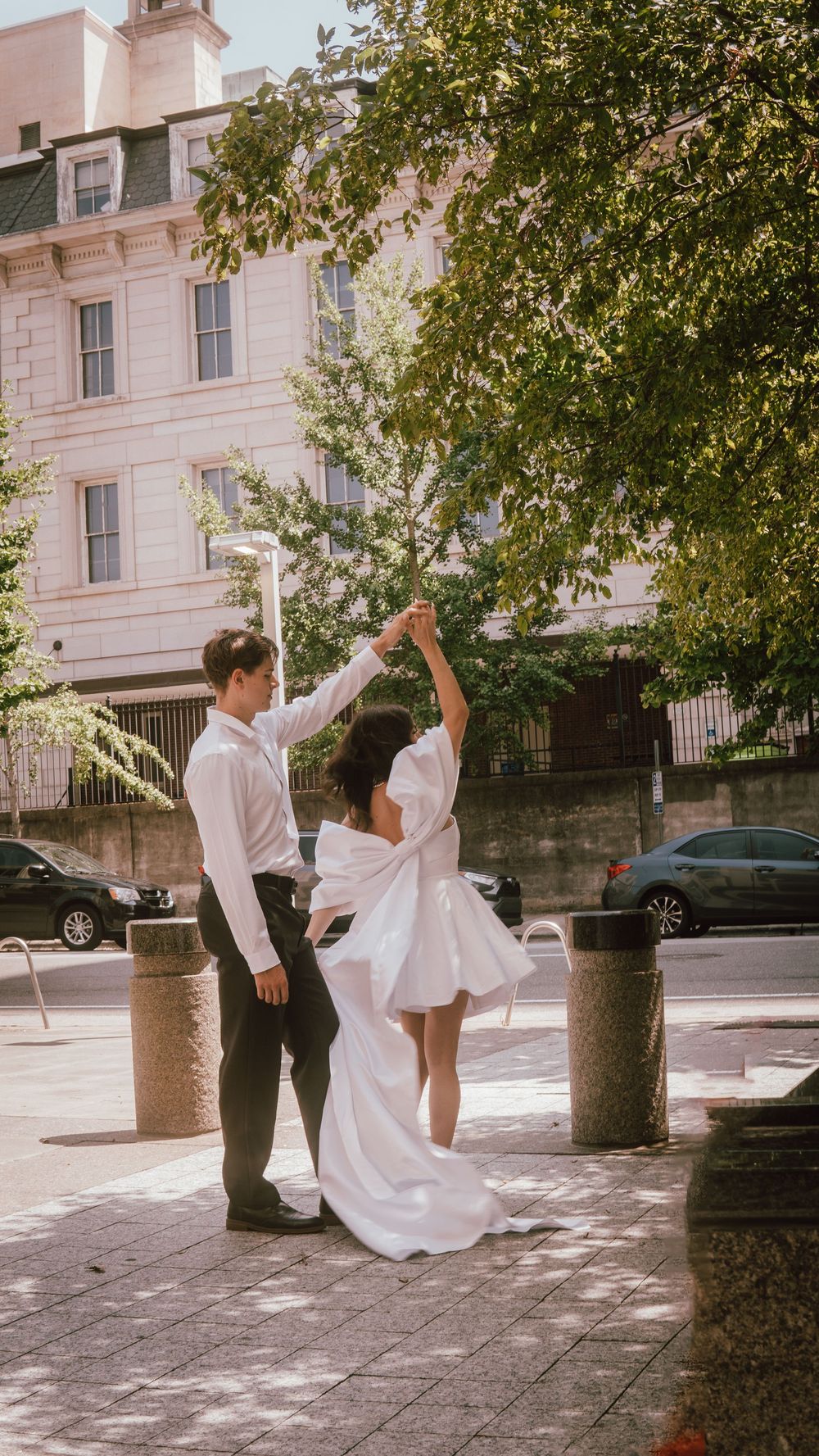 A couple in wedding attire dancing on a city sidewalk, with the bride's white dress flowing gracefully.
