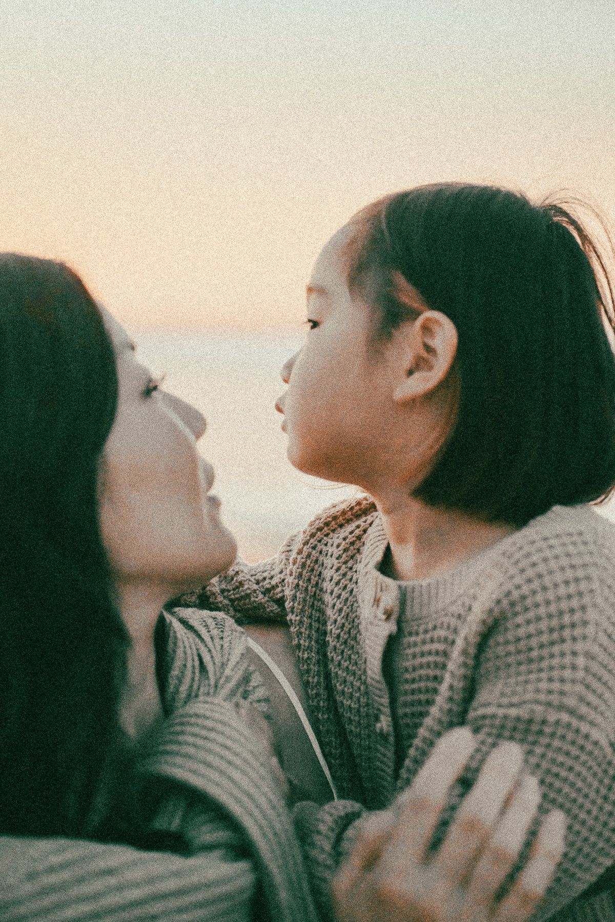Two young Asian women share a tender moment outdoors at sunset, one leaning in for a kiss.