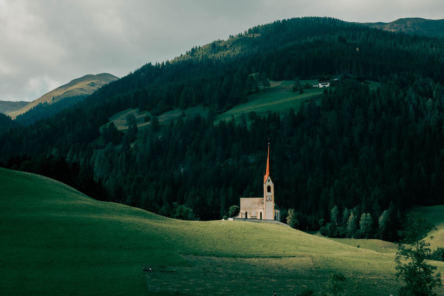 Dramatic Dolomite mountains with jagged rocky peaks, winding road, and moody overcast sky in the Italian Alps.