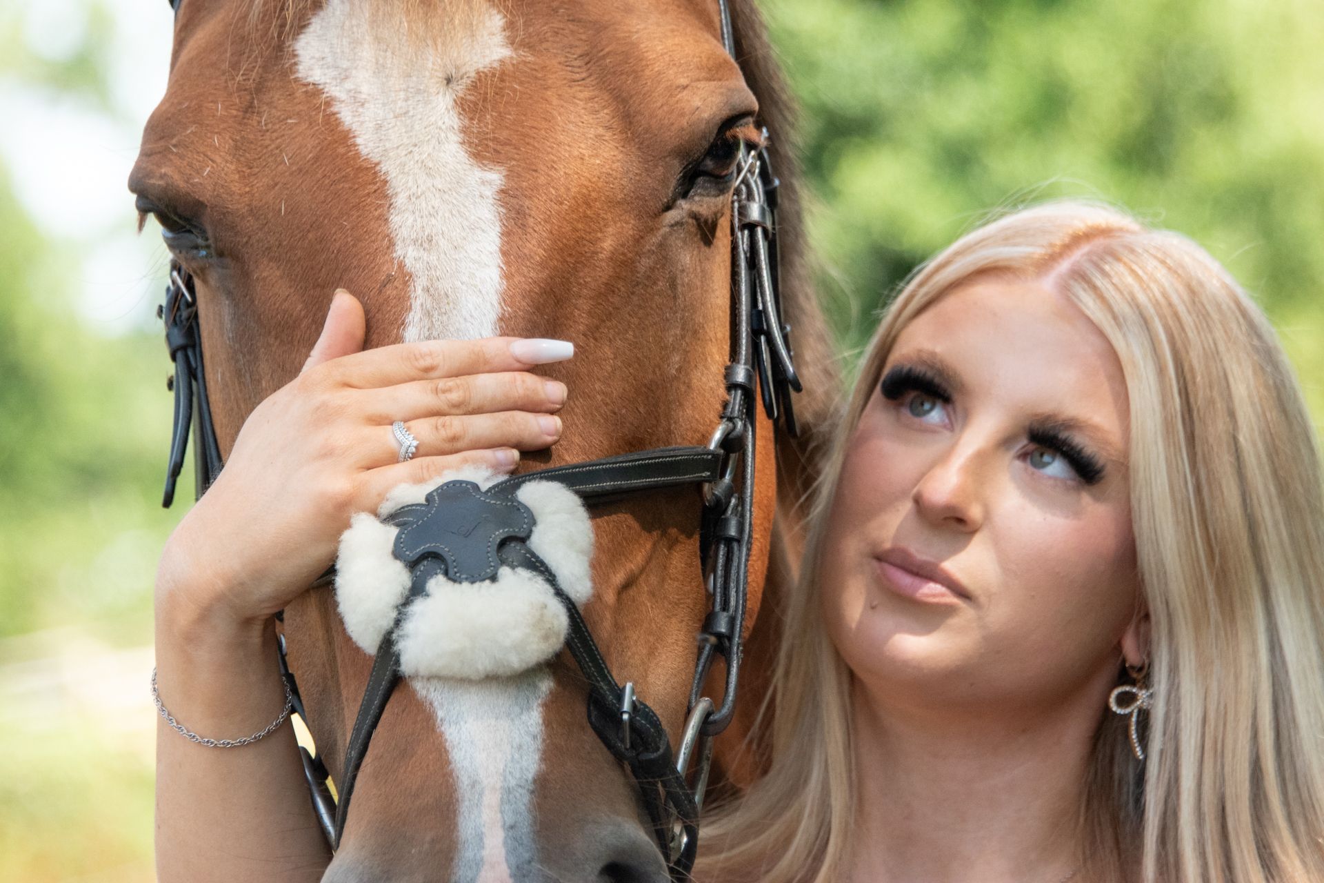 Young woman in white dress smiling affectionately beside a chestnut horse on a country road.