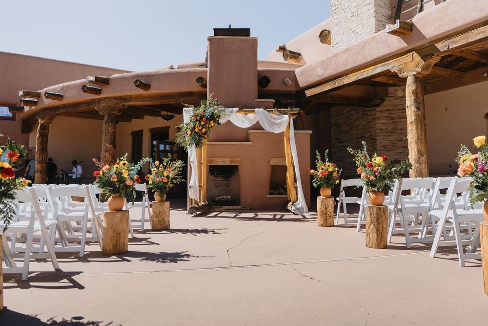 Outdoor wedding ceremony setup with colorful floral arch, white chairs, and Southwestern adobe venue décor.