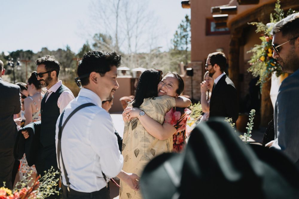 Wedding guests laughing and embracing during joyful outdoor celebration with colorful floral décor.