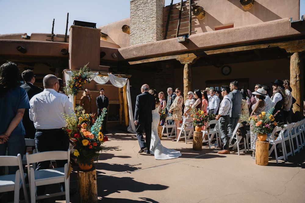 Outdoor wedding ceremony in progress at Southwestern adobe venue with colorful floral arrangements.