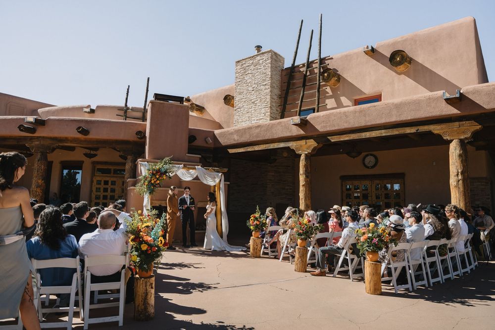 Outdoor wedding ceremony at Southwestern adobe venue with colorful floral arch and seated guests.