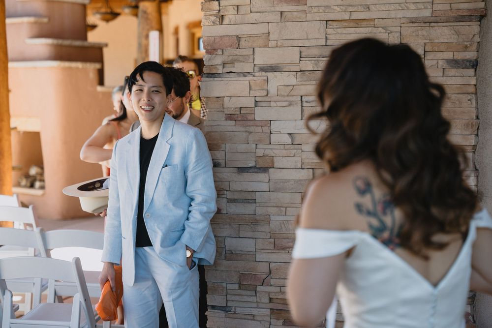 Groom in light blue suit smiling at bride during wedding first look at rustic stone venue.