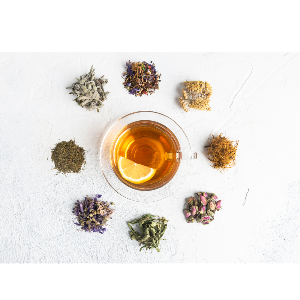 Glass cup of lemon tea surrounded by eight varieties of dried herbal tea blends on a white surface.