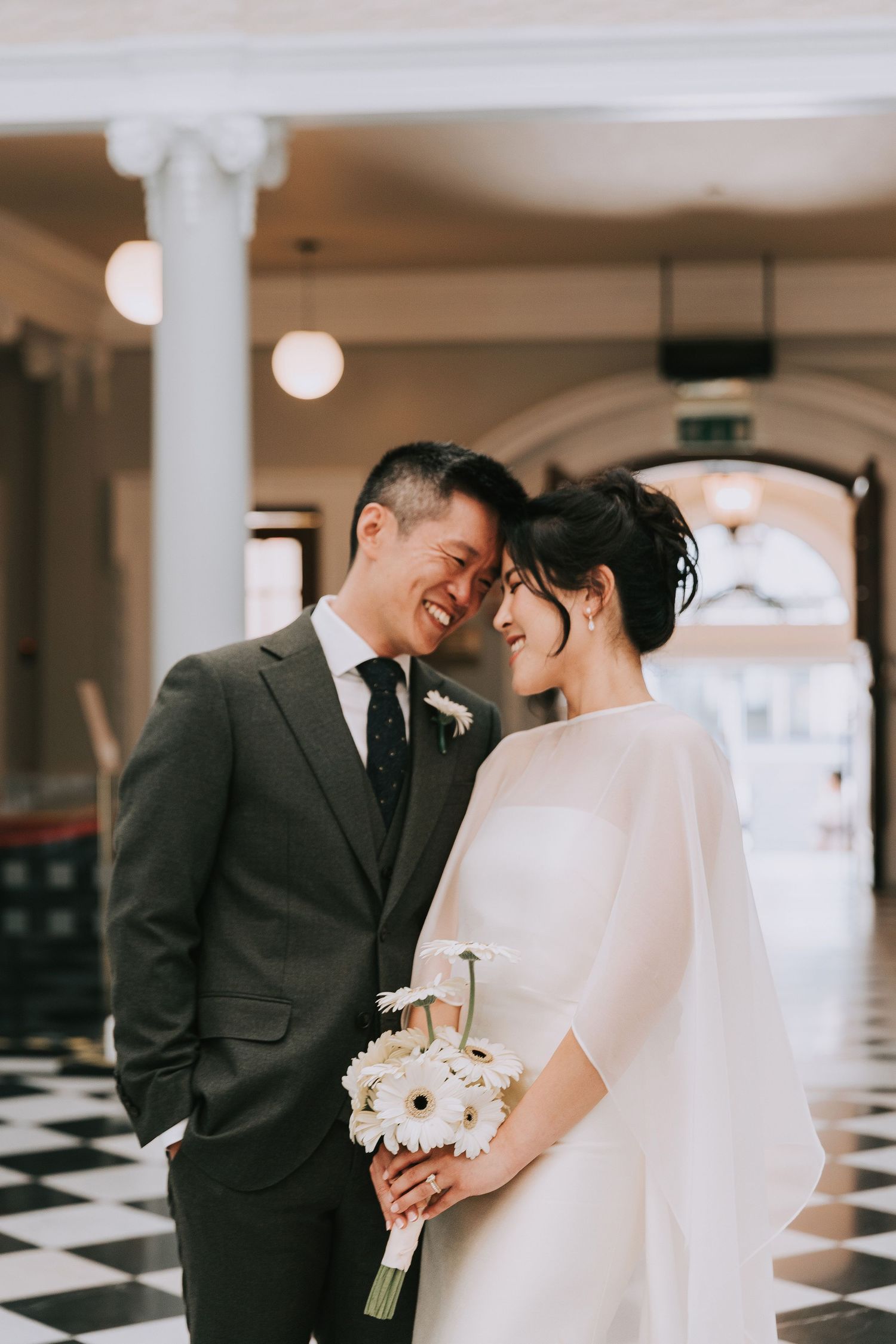 A smiling Asian bride and groom share an intimate moment in the elegant Woolwich Town Hall venue with black and white checkered floors.