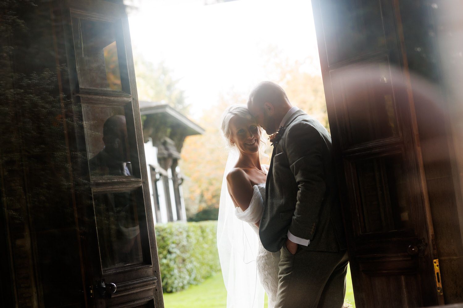 Bride and groom share a romantic moment in a sunlit doorway at an elegant outdoor wedding venue.