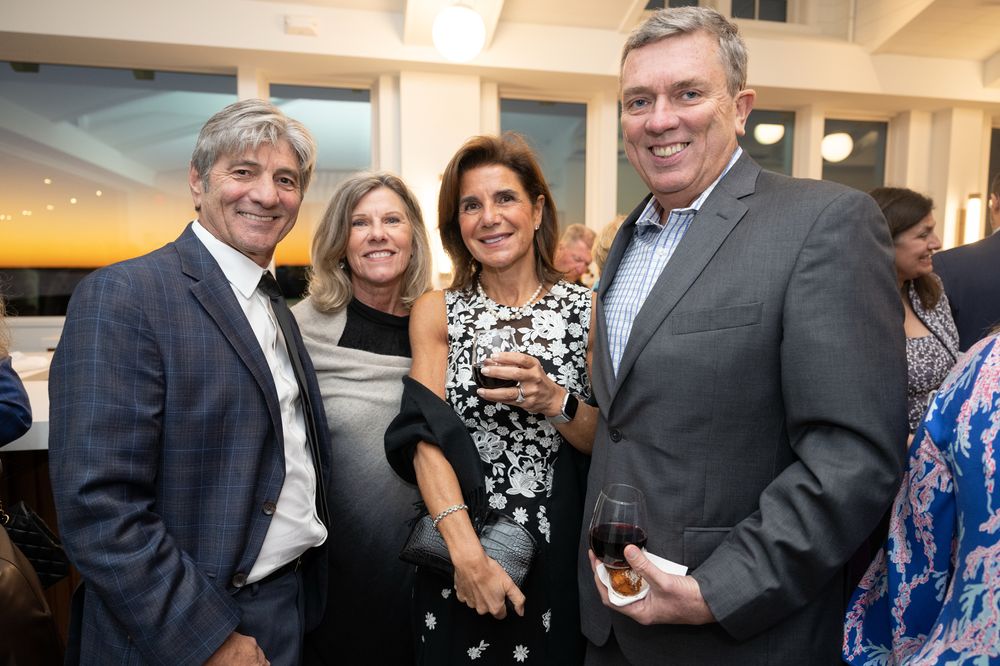 Four adults smiling and socializing at an elegant indoor evening event, holding drinks in a well-lit venue.
