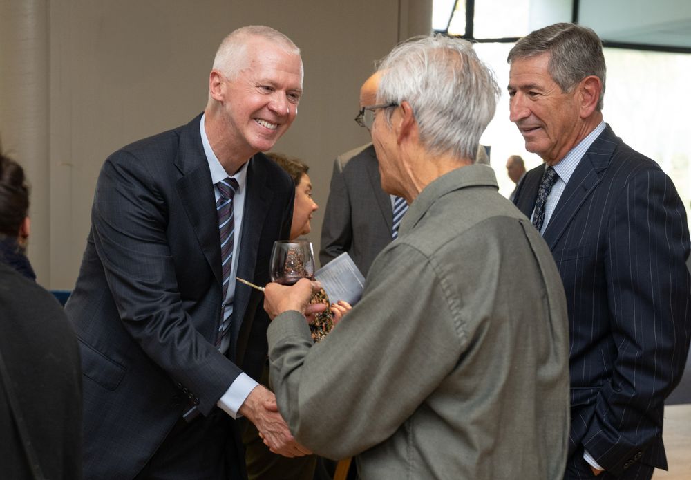Three men in business attire shaking hands and networking at a formal corporate event or reception.