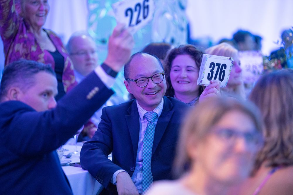 Guests smile and raise numbered bidding paddles at a lively charity auction gala event.