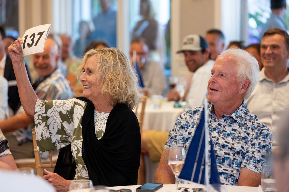 Woman holds up bidding paddle number 137 at a charity auction event while seated with other attendees.