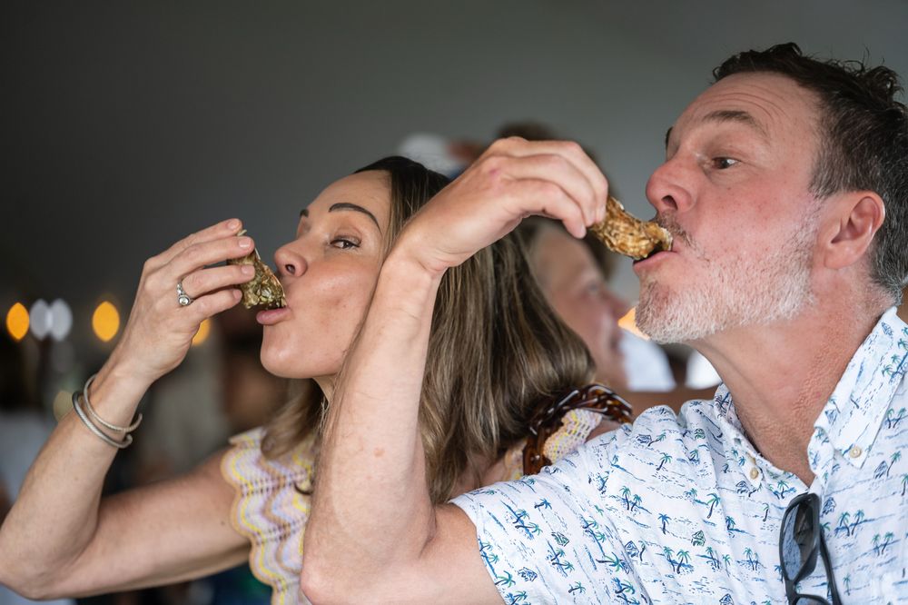 A man and woman enjoy eating seafood together at an outdoor dining event, savoring their food with delight.