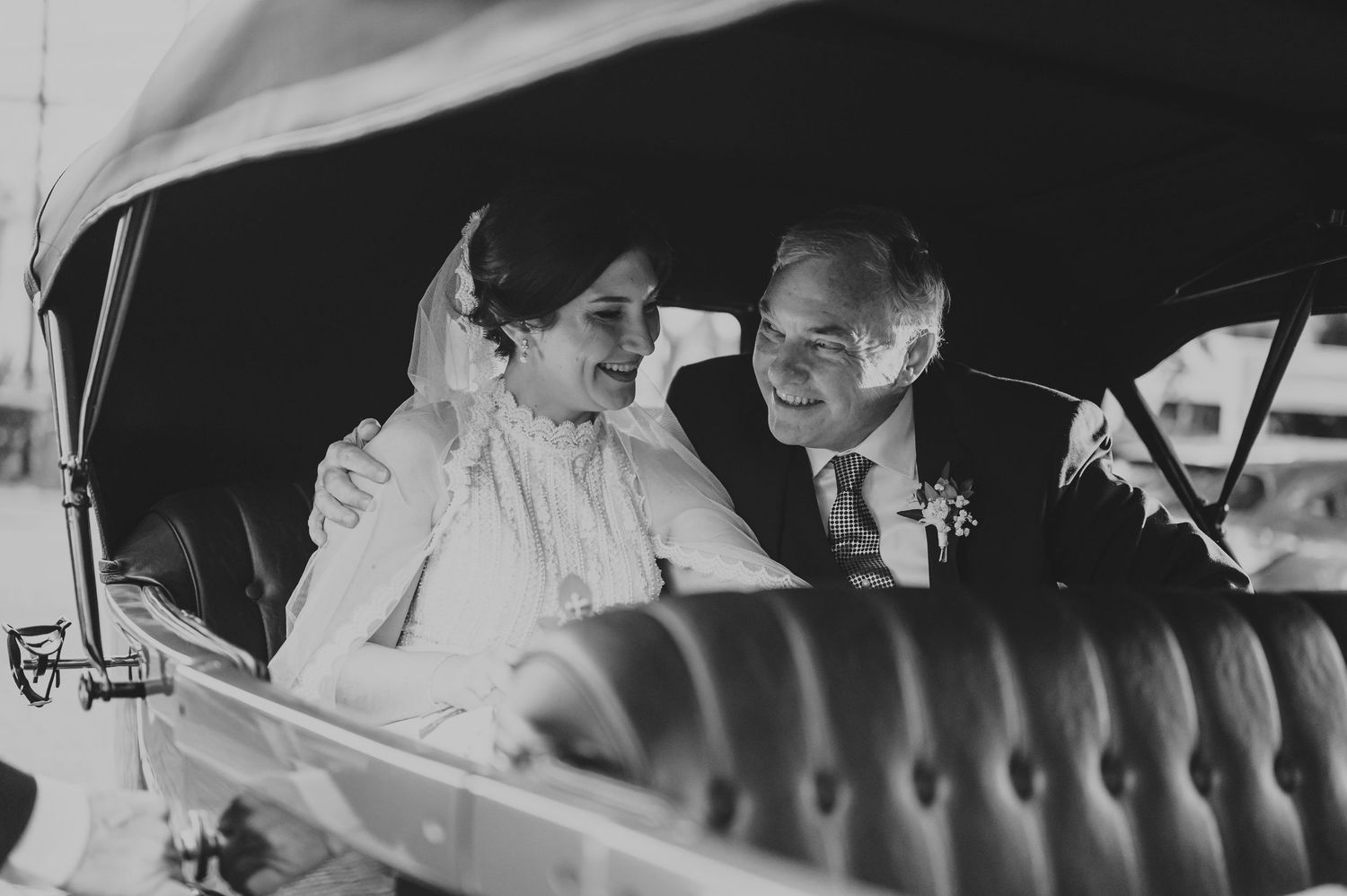 Black and white photo of a bride and groom sharing a tender moment in a vintage car.