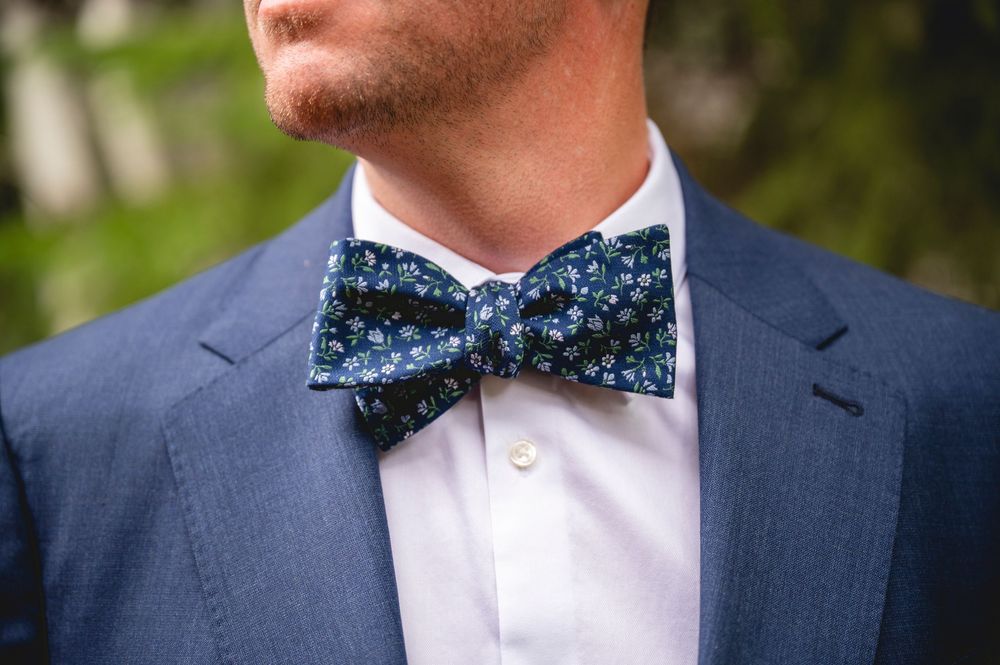 Man in blue suit jacket wearing a navy floral bow tie, close-up shot of elegant wedding attire.