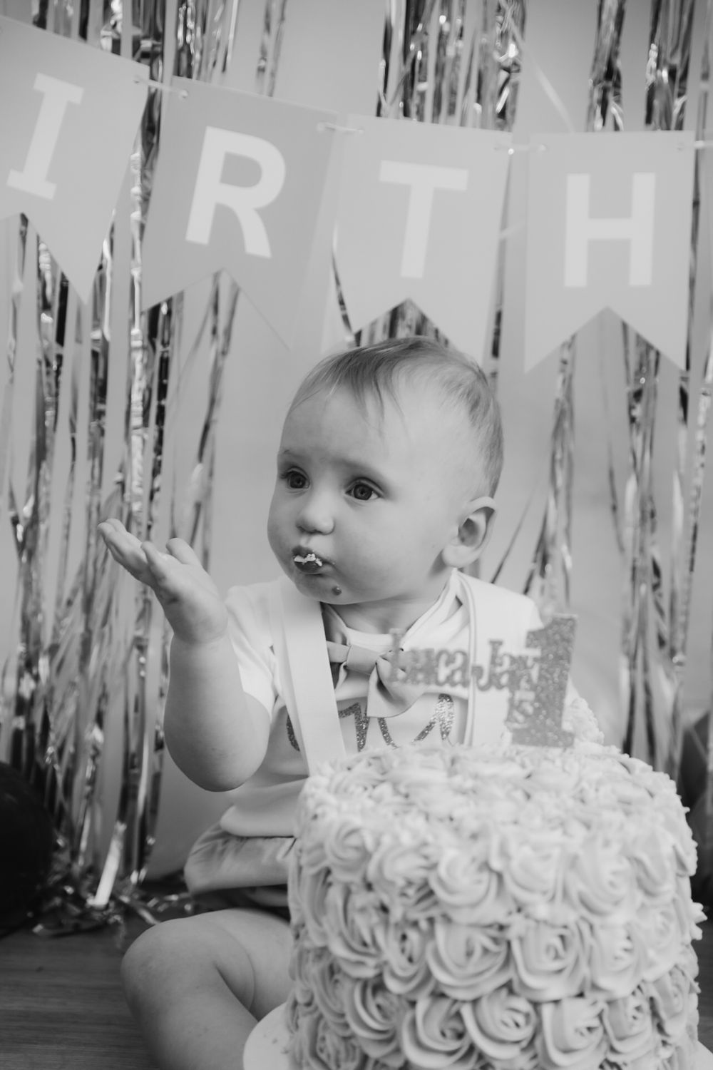 Black and white photo of baby smashing first birthday cake with rose frosting and number one topper.